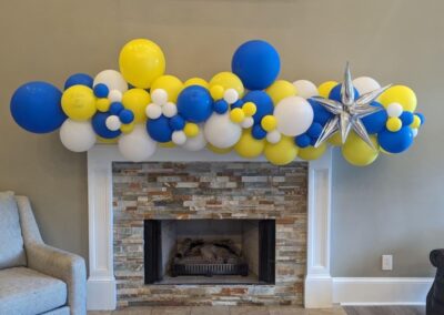 A vibrant blue and yellow balloon garland elegantly drapes above a cozy fireplace, adding a festive touch to the room.