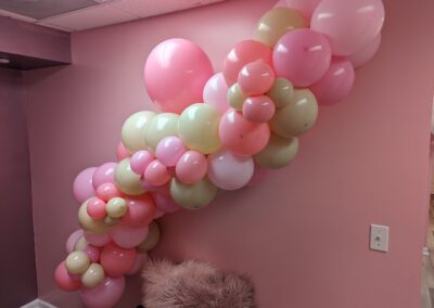 A pink wall adorned with colorful balloons beside a stylish chair, creating a cheerful and inviting atmosphere.