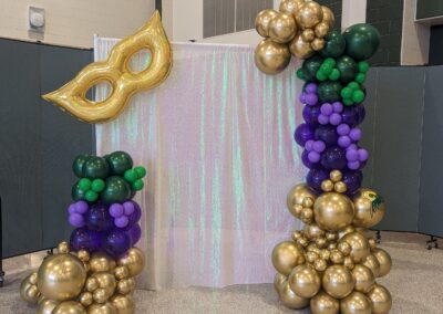 A vibrant balloon arch in Mardi Gras colors, featuring purple, green, and gold balloons, creating a festive atmosphere.